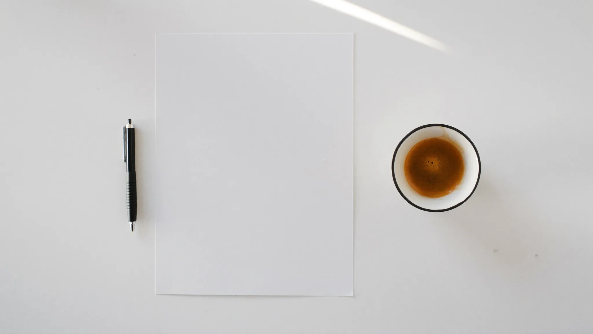 Minimalistisk flat-lay med blankt ark, penn og kaffekopp på hvit flate